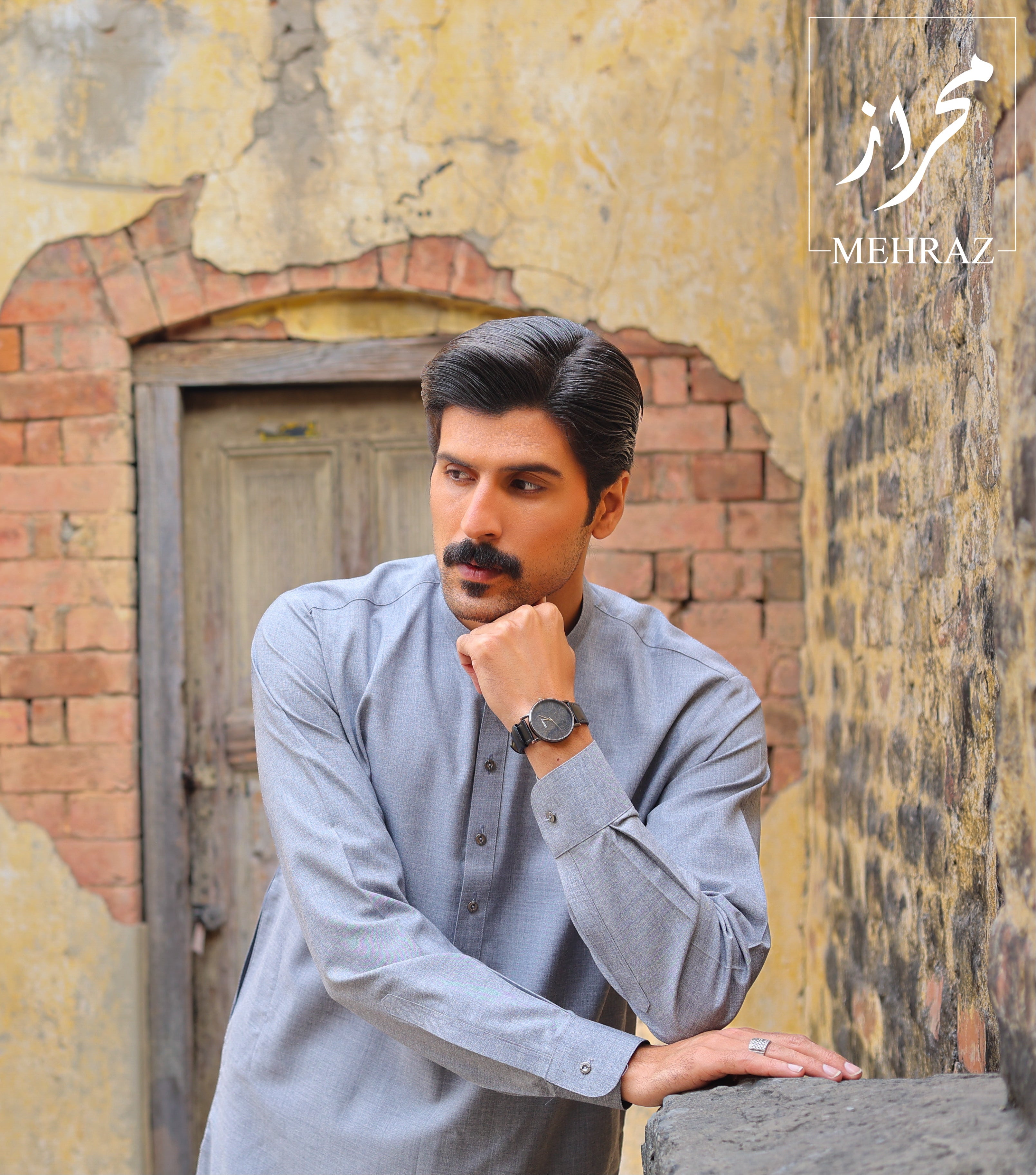 Man in a light gray shirt leaning against a textured wall with a door.